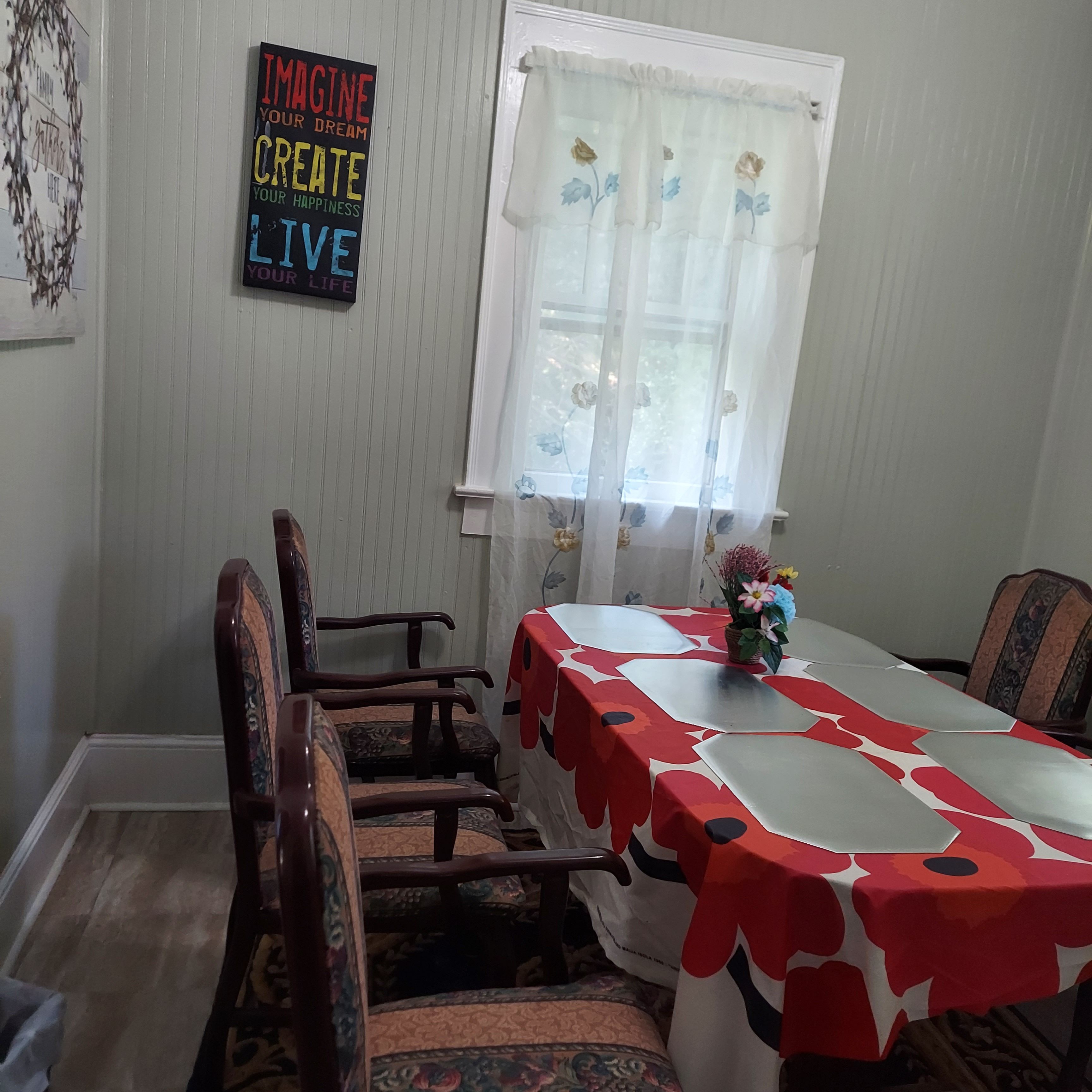 Un coin repas avec une table recouverte d’une nappe rouge et blanche, entourée de chaises à motifs.