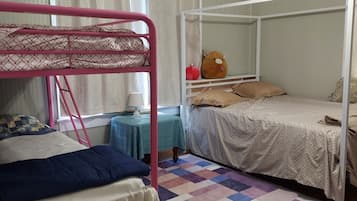 Ein Schlafzimmer mit Etagenbetten, einem kleinen Tisch mit Lampe, einem Teddybären und einem karierten Teppich.