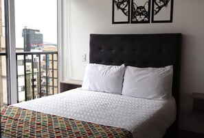 A hotel room with a large bed, white bedding, a patterned throw, and a city view. - Quinta park 43 (Bogotá)