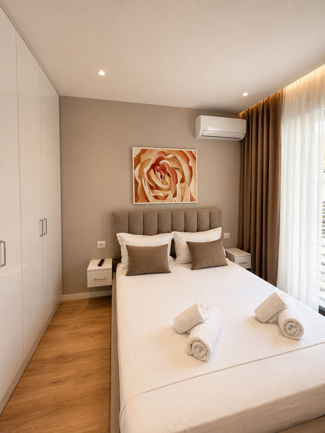 Habitació d'hotel moderna amb un llit gran, una tauleta de nit, aire condicionat fixat a la paret i una finestra amb cortines.
