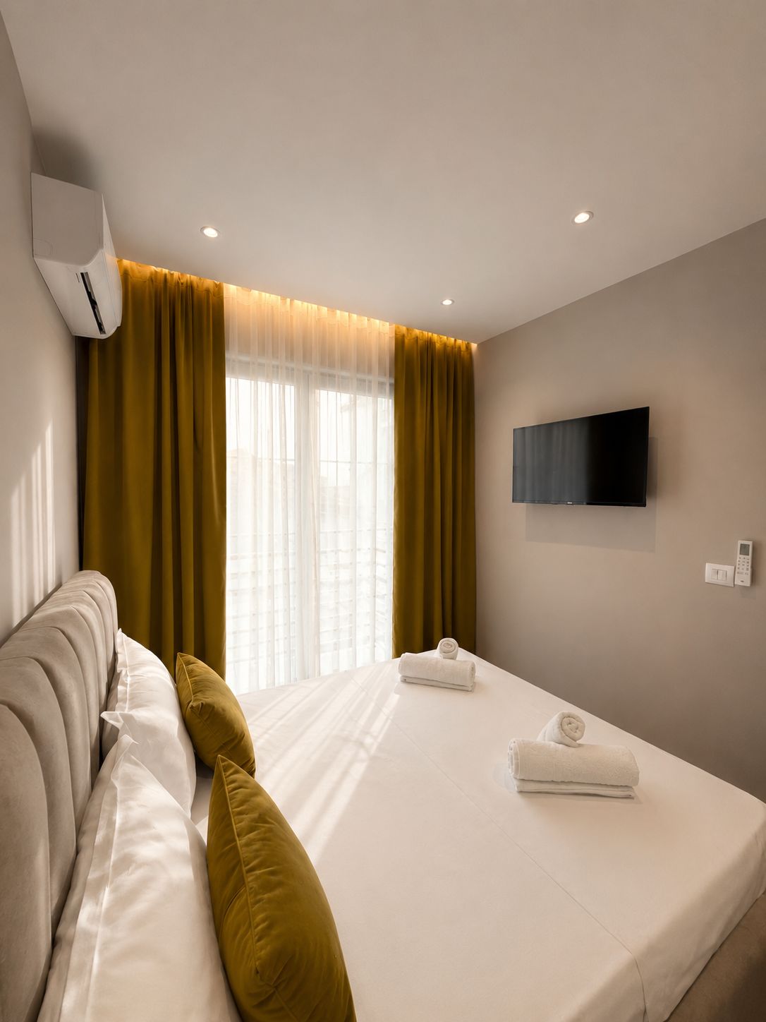 A hotel room with a bed, a sofa, a television, and an air conditioning unit.