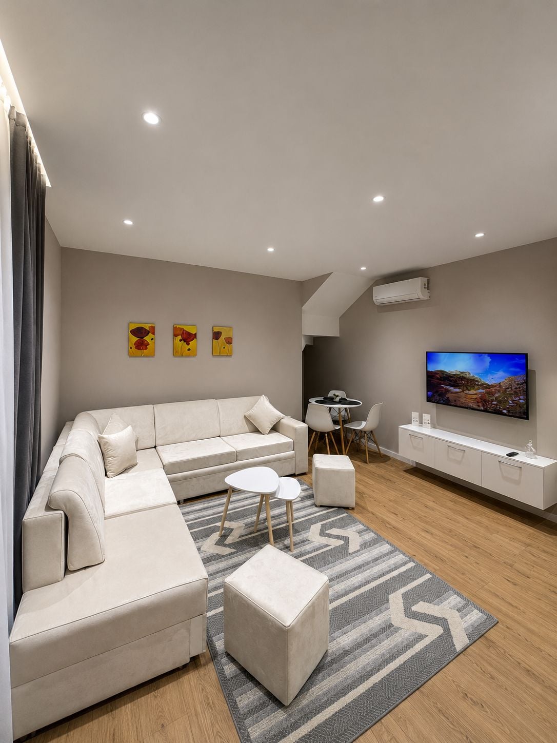 Una sala de estar moderna con un sofá modular, un televisor de pantalla plana, un comedor y una pequeña mesa con sillas.