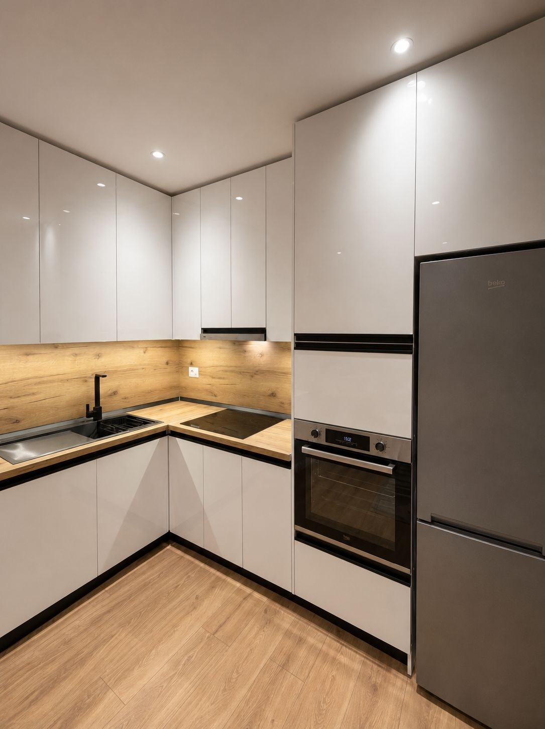 Una cocina moderna con armarios blancos, encimera de madera, pileta de acero inoxidable, horno empotrado y refrigerador.