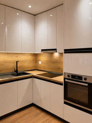 A modern kitchen with white cabinets, a wooden backsplash, a black faucet, and a built-in oven. - ODA Central Stay (Elbasan)