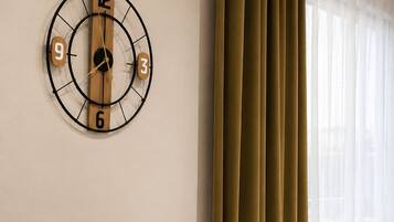 A modern room with a round table, two chairs, a wall clock, and a window with curtains.