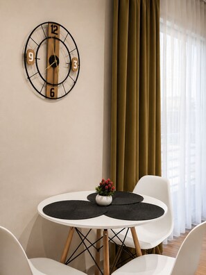 A modern room with a round table, two chairs, a wall clock, and a window with curtains. - ODA Central Stay (Elbasan)