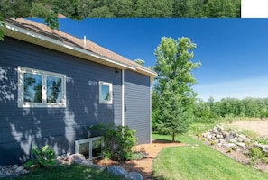 A residential house with a grey siding exterior, a well-maintained lawn, and a large tree in the front yard. - Lakes, Woods & Space.  4BR Home perfectly situated on 6 acres + seasonal cabin. (Brainerd)