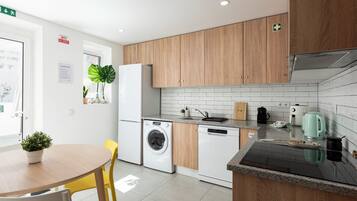 Une cuisine moderne avec des meubles en bois, un lave-linge encastré, une machine à café et une bouilloire posées sur le plan de travail.