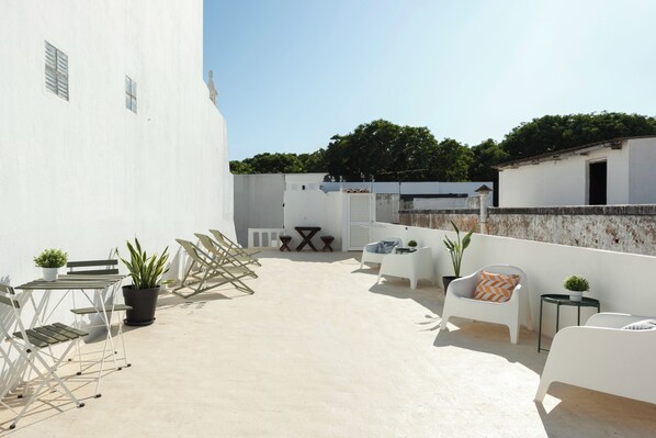 A rooftop terrace with outdoor furniture, potted plants, and a clear view of the surrounding area.