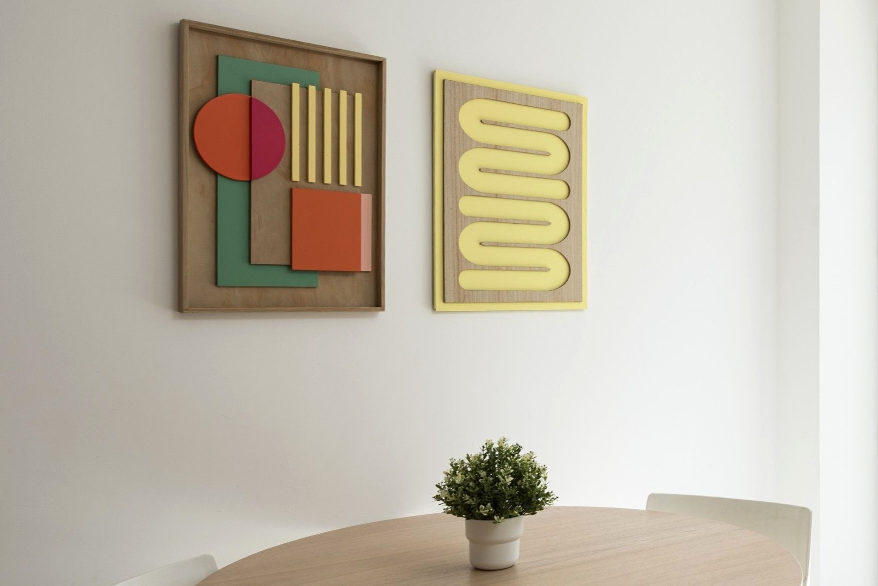 Deux œuvres d’art abstrait sont accrochées à un mur, et une plante en pot est posée sur une table ronde.