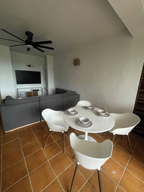 A modern living space with a sofa, a dining table with chairs, a ceiling fan, and a flat-screen TV mounted on the wall.