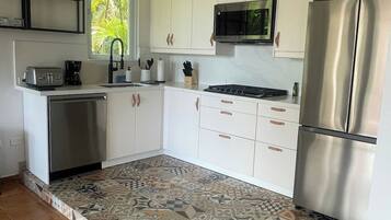 A kitchen with white cabinets, a stainless steel refrigerator, a microwave, and a tiled floor with a geometric pattern.