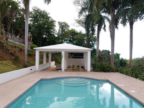 Una piscina con una zona de estar techada y vistas a un paisaje natural.