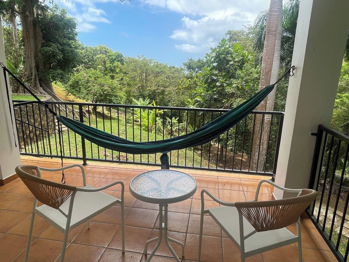 Un balcon avec un hamac, deux fauteuils en osier et une petite table ronde.