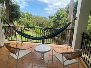 A balcony with a hammock, two wicker chairs, and a small round table.