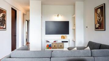 A living room with a grey sofa, a flat-screen TV mounted on a white wall, and a small white entertainment unit below.