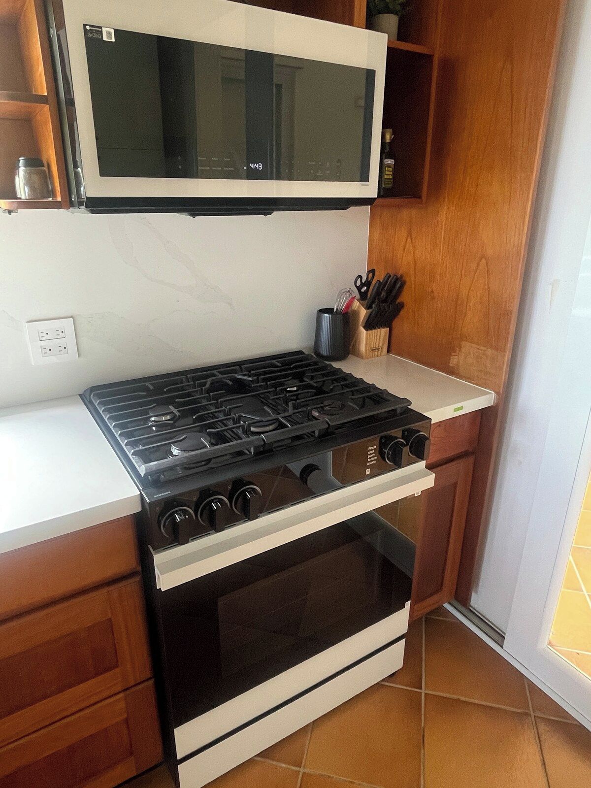 Cozinha equipada com fogão, forno e micro-ondas. Há um balcão com suporte para facas.