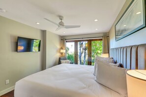Ein Hotelzimmer mit Bett, Deckenventilator, Fenster mit Vorhängen und einem Bild an der Wand.