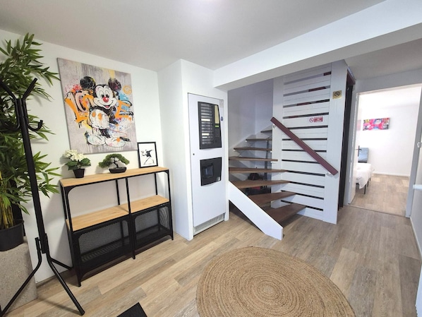 Una escala de fusta amb barana que condueix a una habitació amb un llit i una obra d'art penjada a la paret.