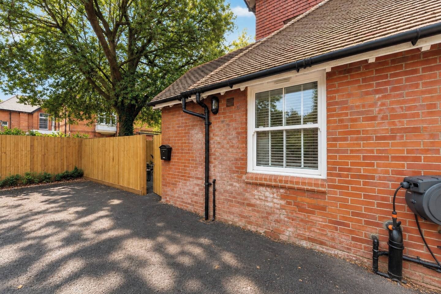 A brick house with a window, a wooden fence, and a black pipe on the ground.
