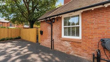 A brick house with a window, a wooden fence, and a black pipe on the ground.