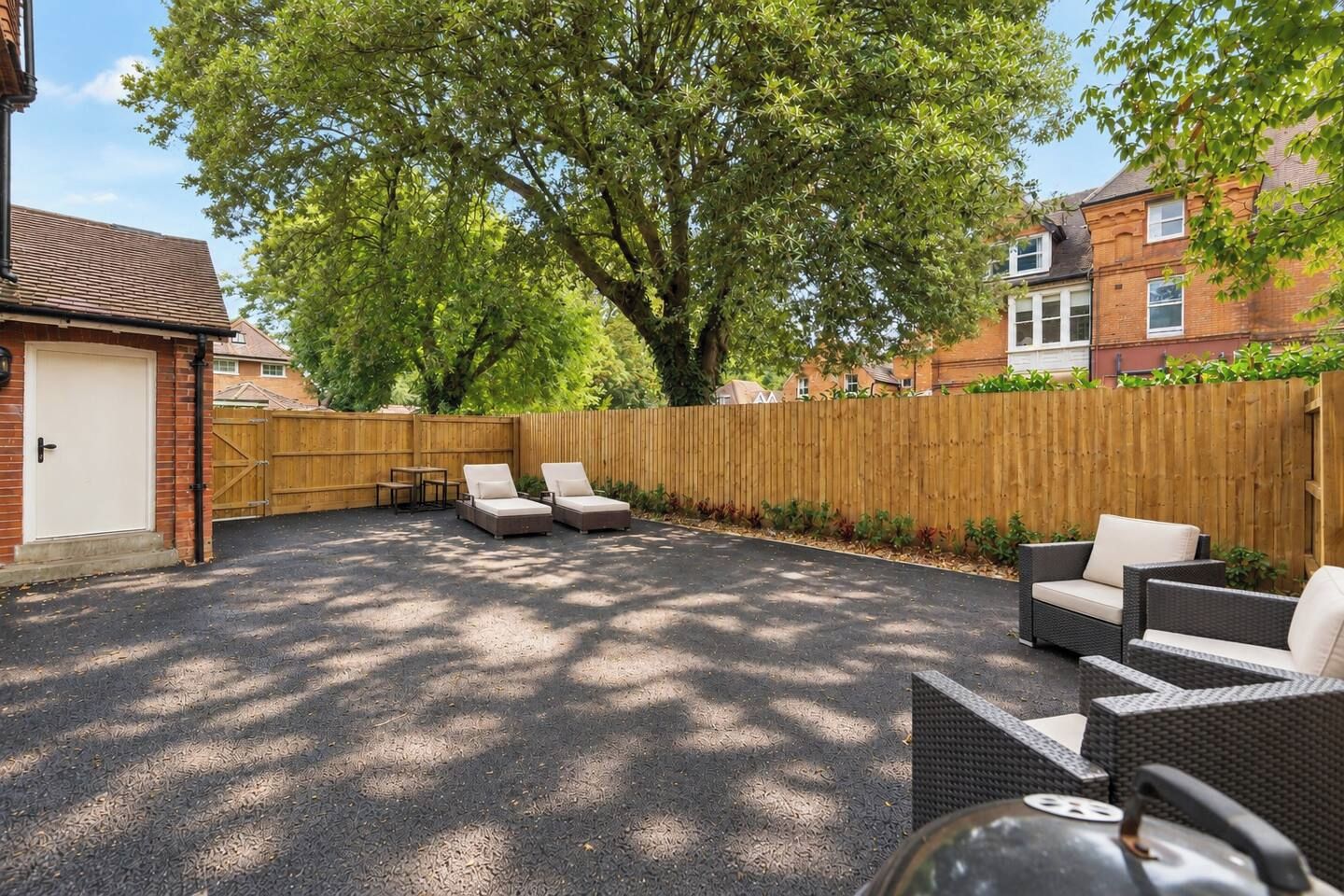 A backyard with a paved area, two lounge chairs, a table, and a wooden fence.