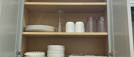 A kitchen cabinet with multiple shelves containing plates, bowls, and cups.