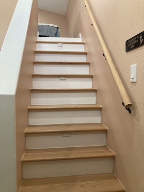Una escalera con escalones de madera y barandilla, un letrero de precaución en la pared y un interruptor de luz.