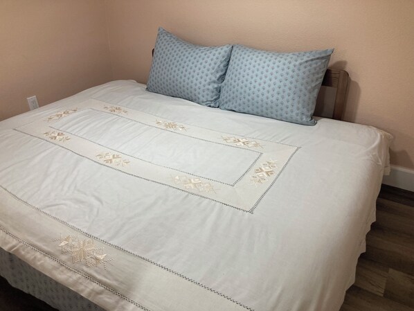 Ein Bett mit weißer Bettdecke mit goldener Stickerei und einem blauem Kopfkissen mit Punktmuster.
