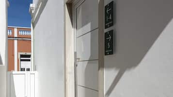 A building entrance with a white door and a wall-mounted sign indicating room numbers 1-4 and 5.