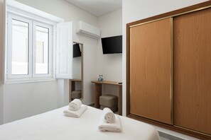 A hotel room with a bed, a TV mounted on the wall, a wardrobe, and a window with blinds.