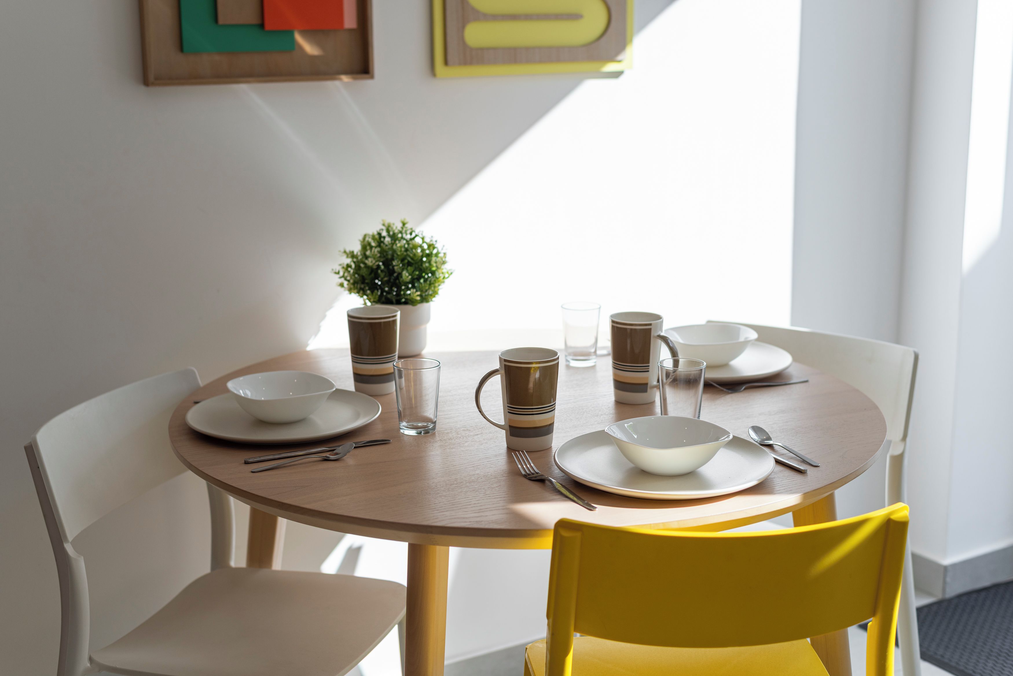 A dining table set with plates, bowls, cups, and cutlery, a potted plant, and a yellow chair.