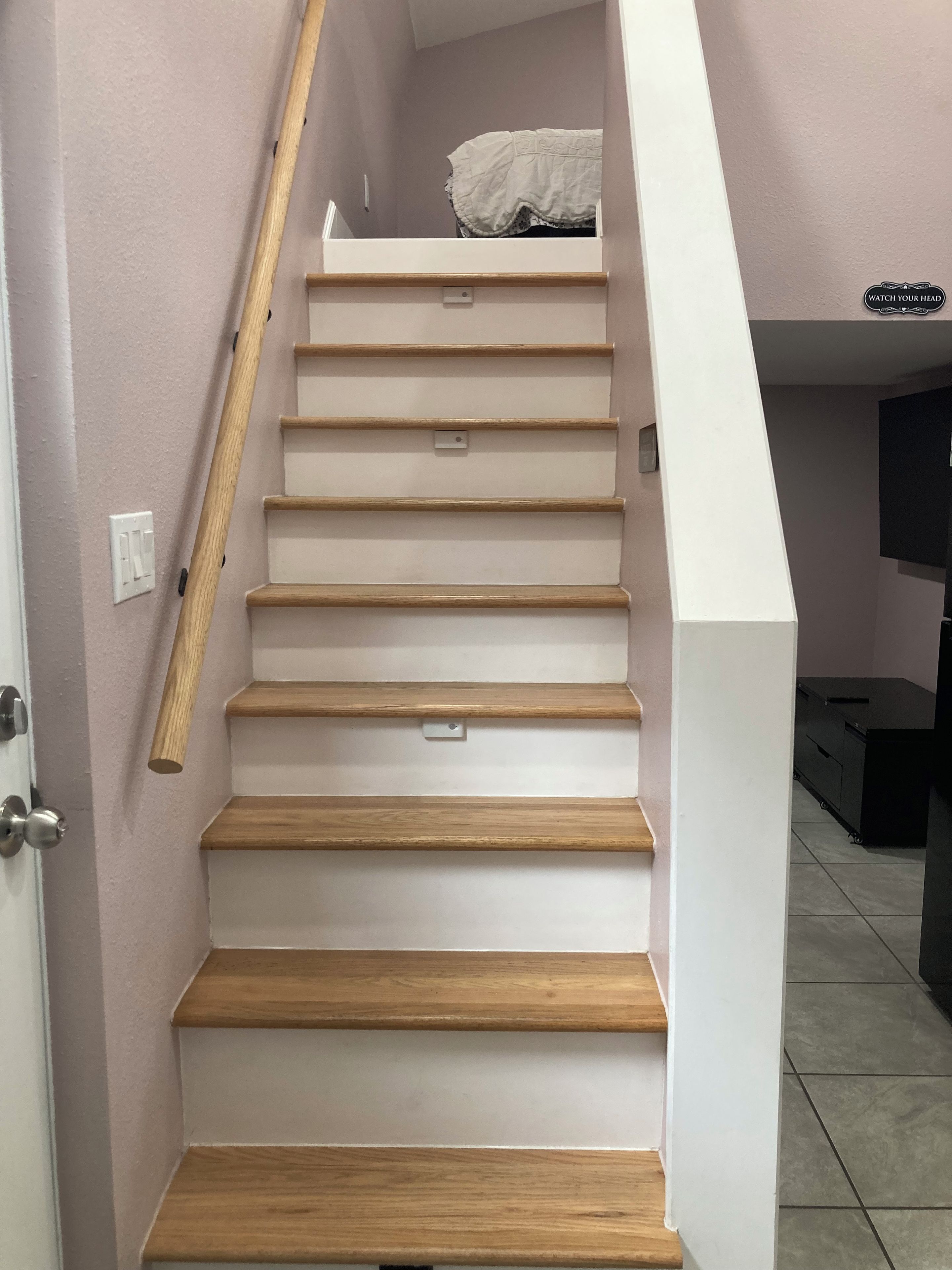 Eine Treppe mit Holzhäuschen und einer weißen Wand, die zu einer Zwischenebene mit einem schwarzen Schrank führt.