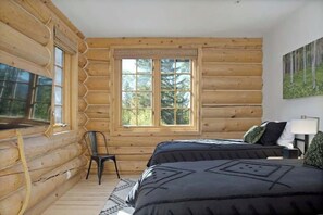 Ein Schlafzimmer in einer Blockhütte mit zwei Betten, einem Fenster und einem Bild an der Wand.