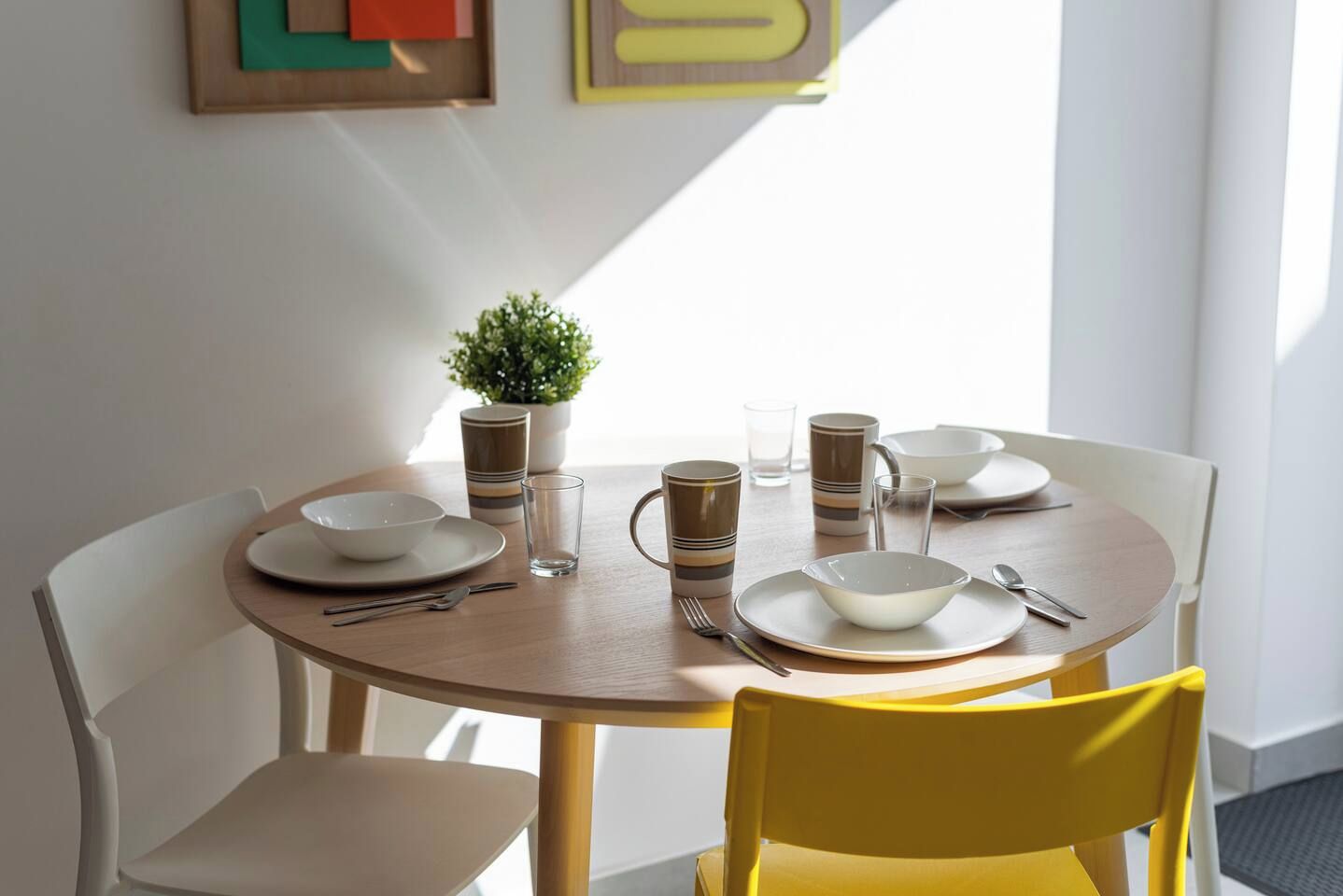 Een ronde eettafel met borden, kommen en mokken, omringd door stoelen.