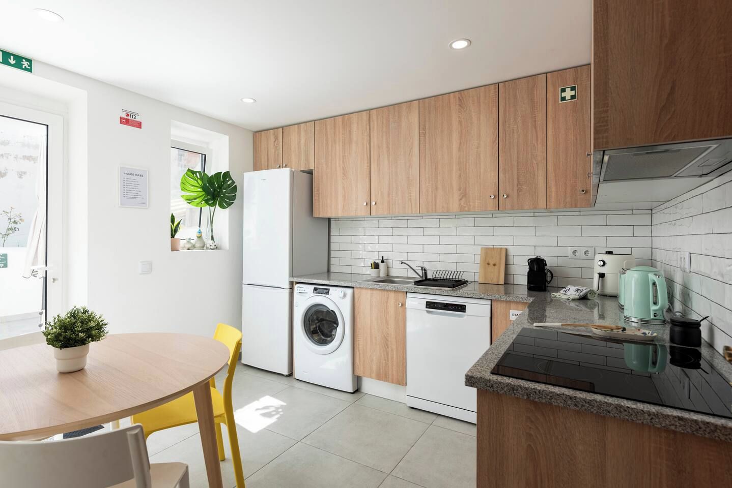 Een moderne keuken met houten kastjes, een wasmachine, een koffiezetapparaat en een eethoek met een tafel en stoelen.
