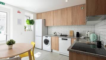Een moderne keuken met houten kastjes, een wasmachine, een koffiezetapparaat en een eethoek met een tafel en stoelen.