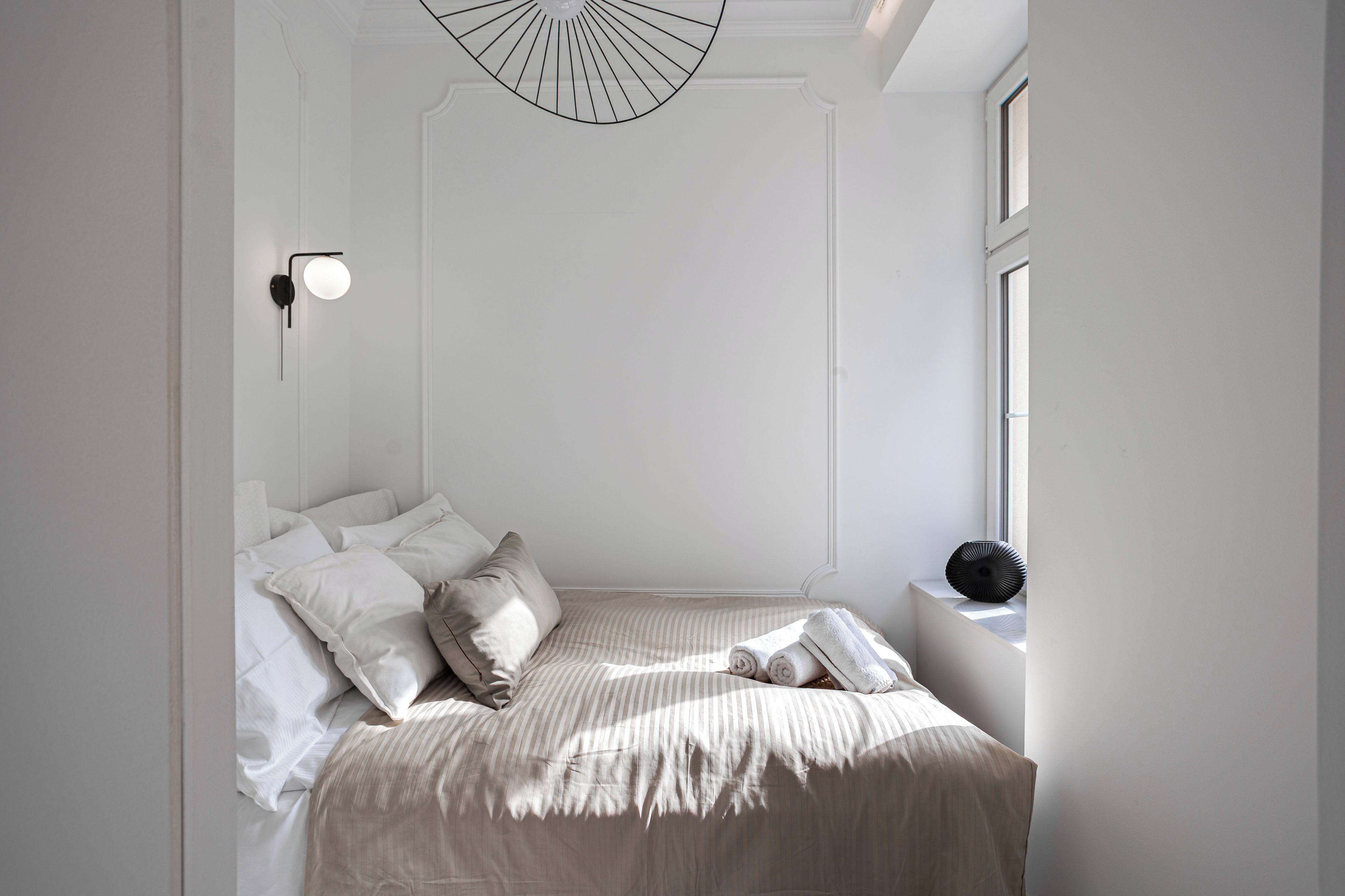 Un dormitorio minimalista con cama, almohadas, una mesita de noche y una lámpara de pared.
