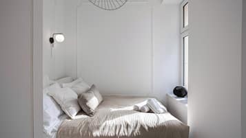 Un dormitorio minimalista con cama, almohadas, una mesita de noche y una lámpara de pared.