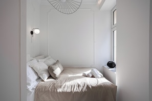 A minimalist bedroom with a bed, pillows, a bedside table, and a wall-mounted light fixture. - Nowoczesne Studio w Kamienicy (Poznań)