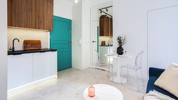 Una cocina moderna con armarios de madera, una puerta color turquesa y un comedor con mesa blanca y sillas transparentes.