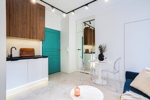 A modern kitchen with wooden cabinets, a teal door, and a dining area with a white table and clear chairs. - Nowoczesne Studio w Kamienicy (Poznań)