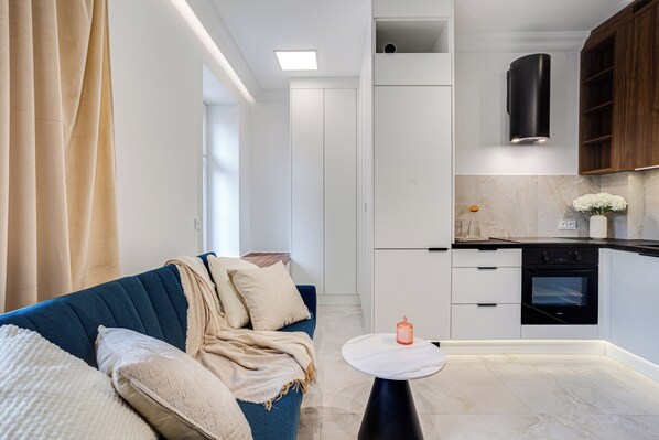 A modern kitchen with white cabinets, a black oven, and a small round table with a candle. - Nowoczesne Studio w Kamienicy (Poznań)