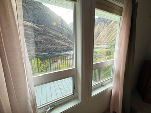 Ein Zimmer mit drei Fenstern, das auf eine gebirgige Landschaft und einen Fluss blickt.