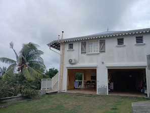 A two-story building with a covered porch, a garage, and a small outdoor seating area. - Spacious apartment (Le Marin)