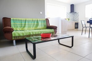 Ein Wohnzimmer mit einer Couch, einem Glastisch und einer Küche im Hintergrund.