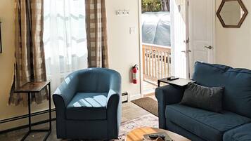 Una sala de estar con un sillón azul, un sofá azul, una mesita de centro pequeña y un tapete estampado.