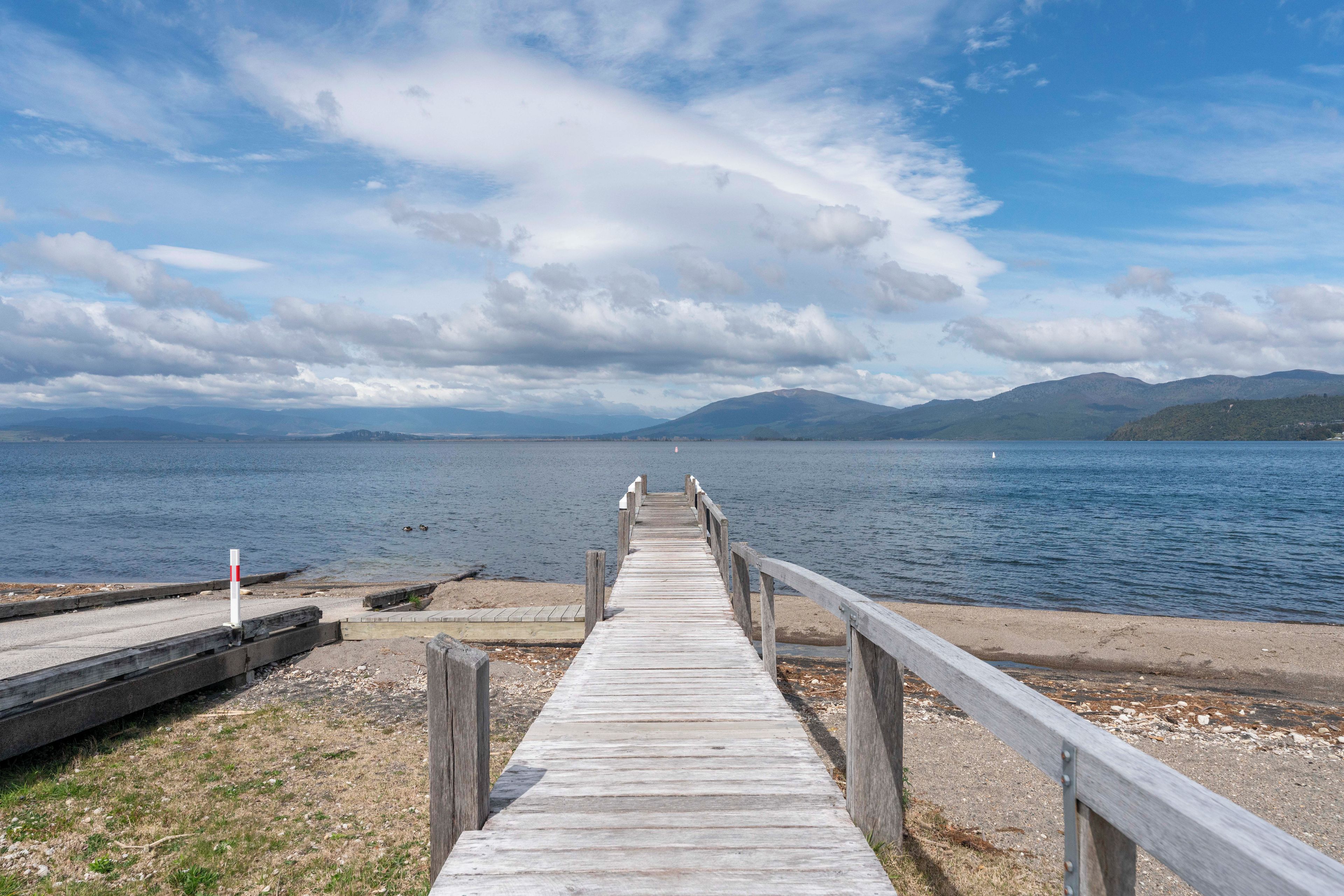 A wooden pier extending into a calm lake with mountains in the background.
