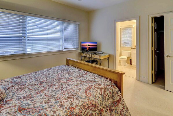 A bedroom with a bed, a desk with a computer, a television, and a bathroom visible through an open door. - Steps From The Ocean, Luxury Home, Private Pool! (Hilton Head Island)
