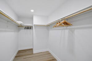 Una habitación pequeña con paredes blancas, suelo de madera, una lámpara en el techo y dos perchas de madera en una barra.